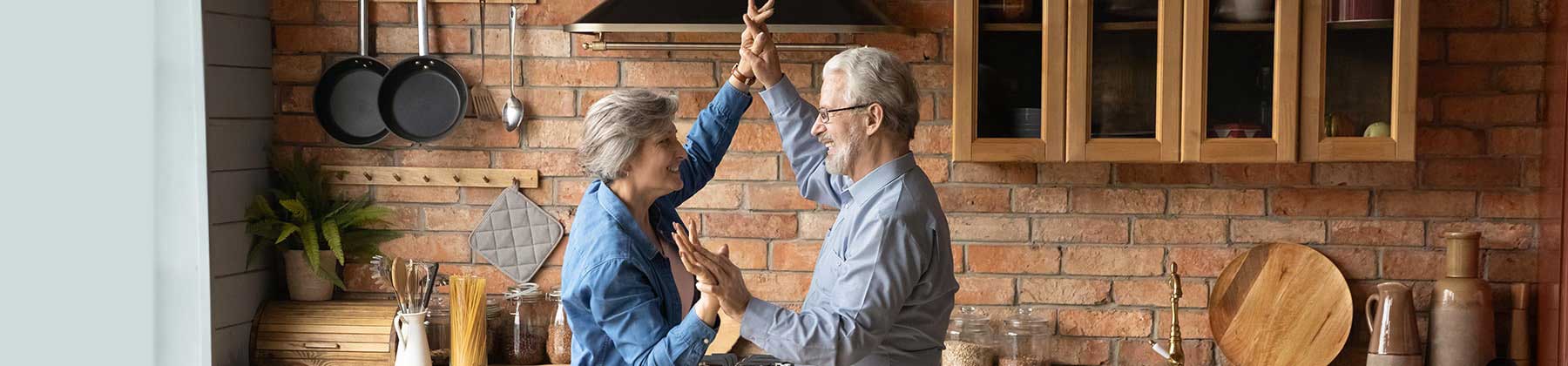 Coppia uomo e donna in età pensionabile accennano gioisamente un passo di danza nella loro nuova cucina