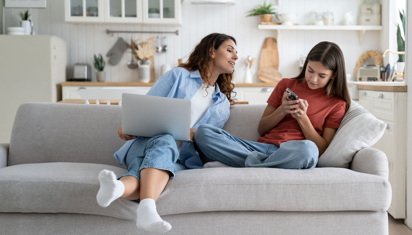 Madre e figlia sedute sul divano con un laptop e uno smartphone
